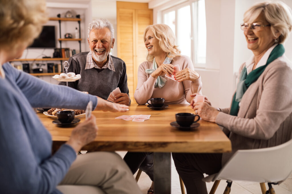 cheerful senior friends playing cards while gathering at home.